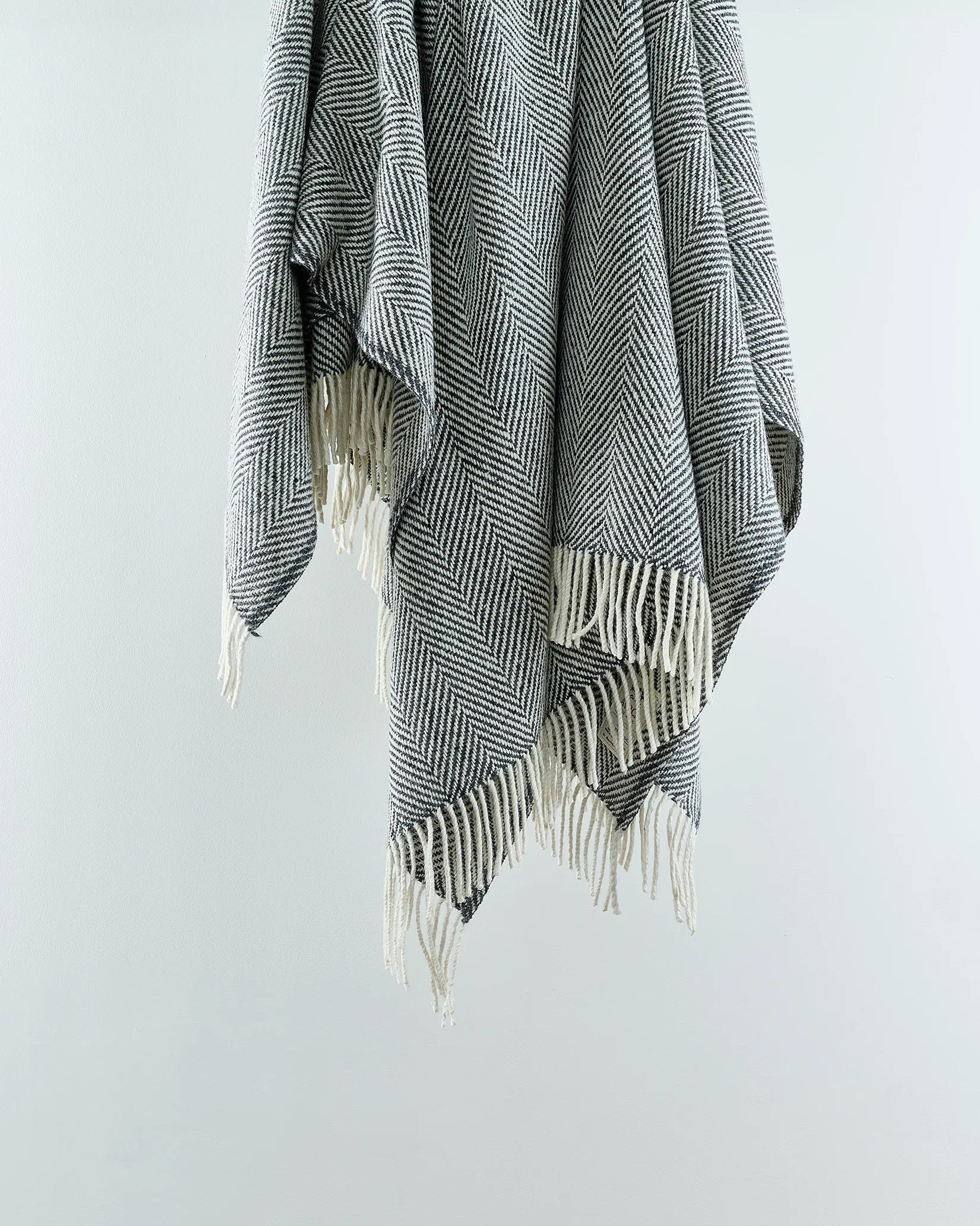 A grey wool herringbone throw with fringes displayed on a white background