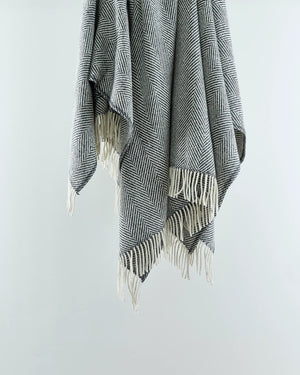 A grey wool herringbone throw with fringes displayed on a white background