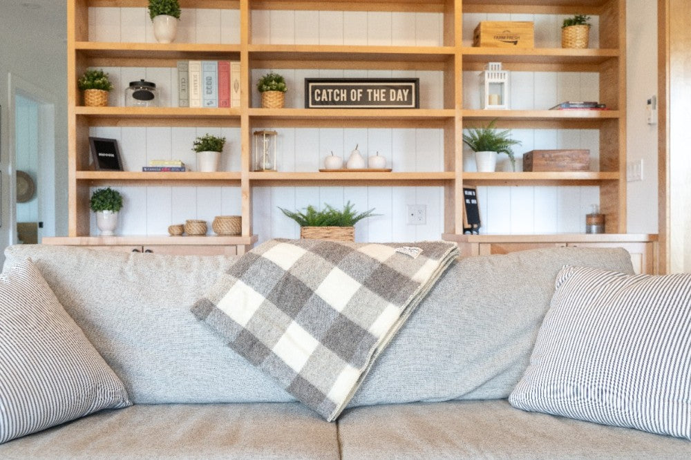 A dark grey and white wool throw draped over the back of a beige sofa, with a cozy living room scene in the background.