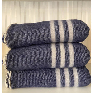 Navy dark blue throw blanket with natural white stripes, rolled up and placed against a light background.