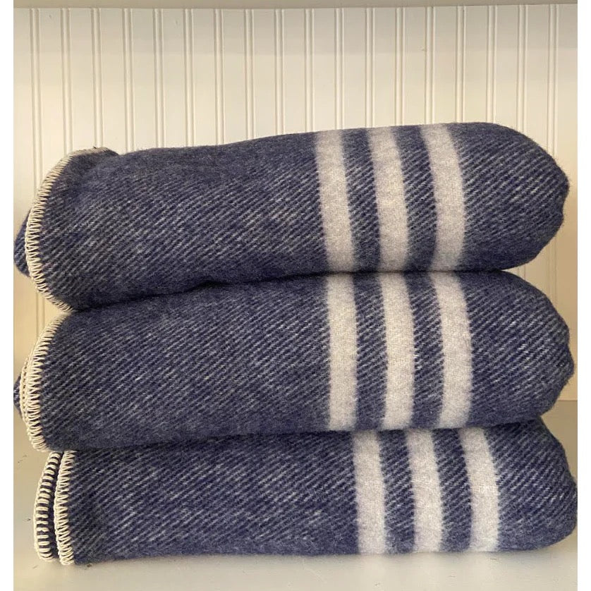 Navy dark blue throw blanket with natural white stripes, rolled up and placed against a light background.