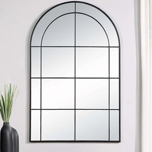 Architectural mirror with grid design on a white wall, next to a vase with plants.