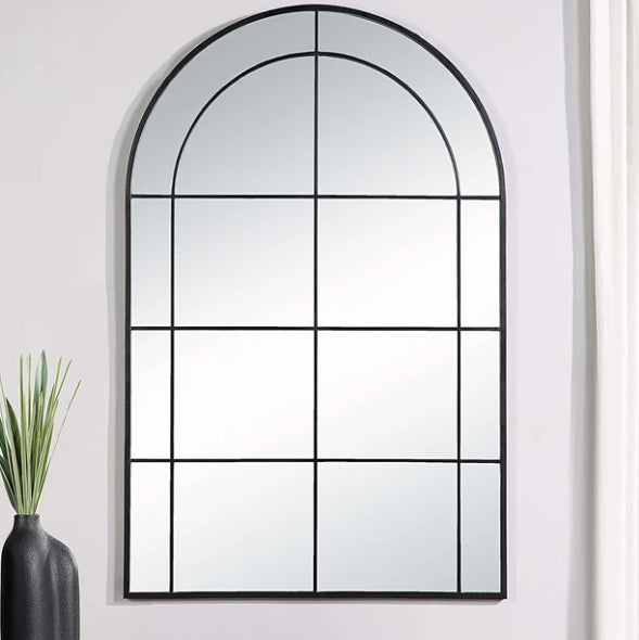 Architectural mirror with grid design on a white wall, next to a vase with plants.