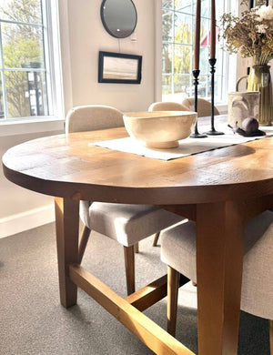 Wooden dining table with chairs in a bright room with large windows.