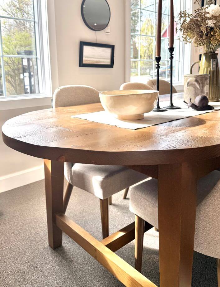 Wooden dining table with chairs in a bright room with large windows.