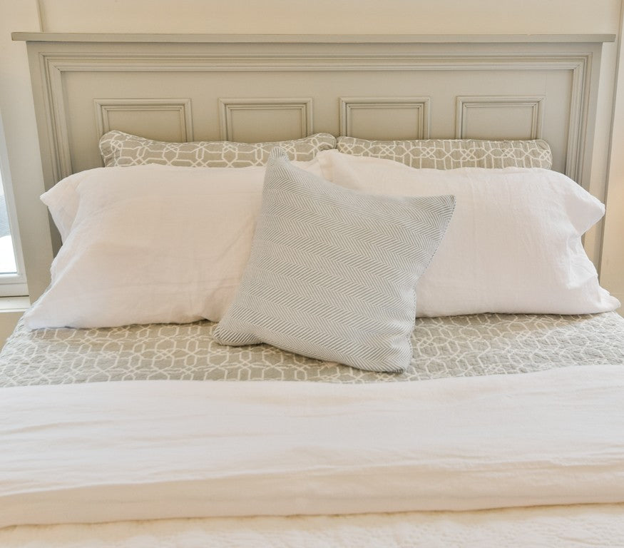 Neatly made bed with white and gray pillows against a neutral headboard.
