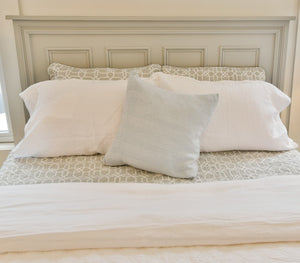 Neatly made bed with white and gray pillows against a neutral headboard.