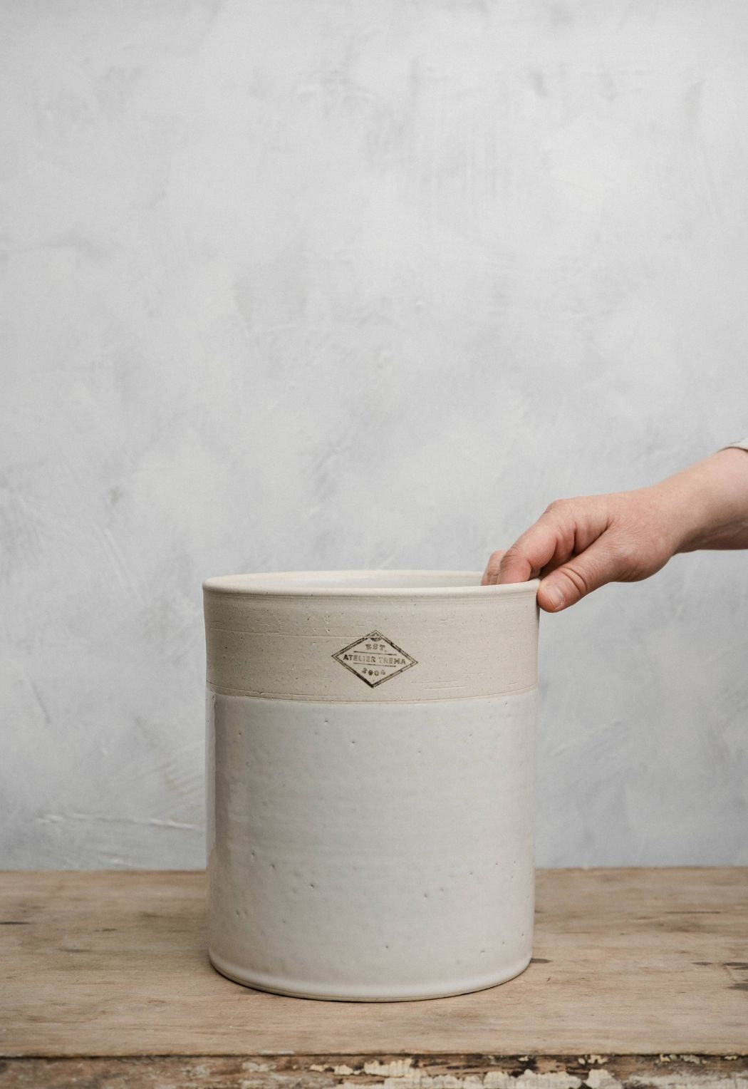 Ceramic utensil pot with a hand holding it against a gray background