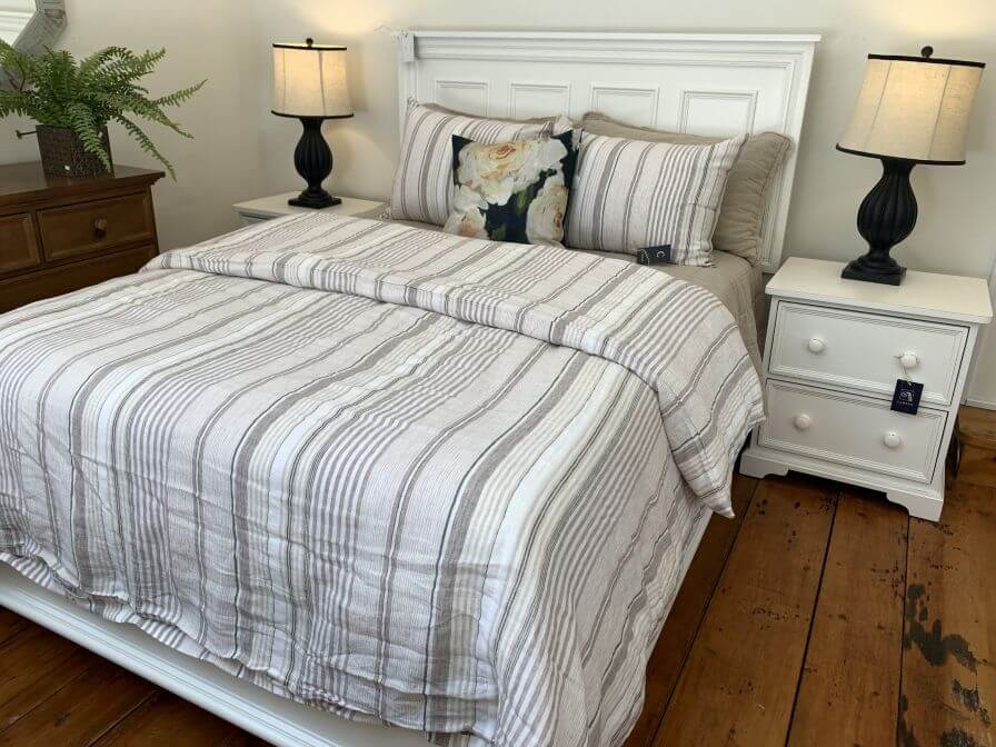 Bedroom set with a neatly made bed, striped bedding, and two nightstands with lamps.