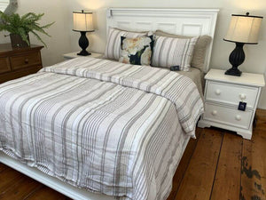 Bedroom set with a neatly made bed, striped bedding, and two nightstands with lamps.