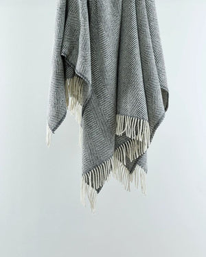 A grey wool herringbone throw with fringes displayed on a white background