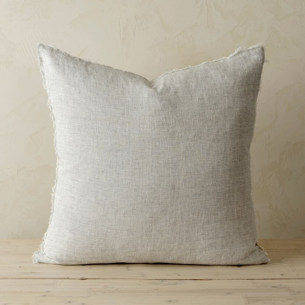 Large grey striped pillow on a wooden surface with a neutral background