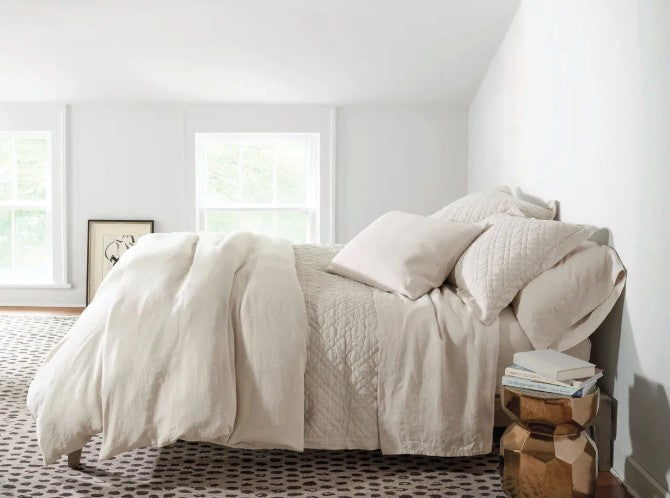 linen bedding on a bed in a loft room in Quebec with a rug, photo against the wall and wooden table with books