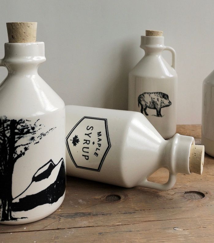 Quaint porcelain maple syrup jugs with corks stand on a wooden board with one lying on the side.