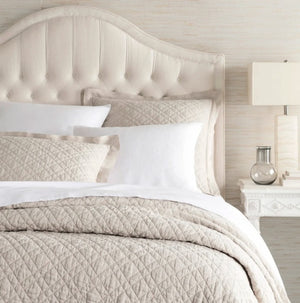 natural quilt of linen on a natural coloured bed with pillow shams and a bedside table with a vase and light