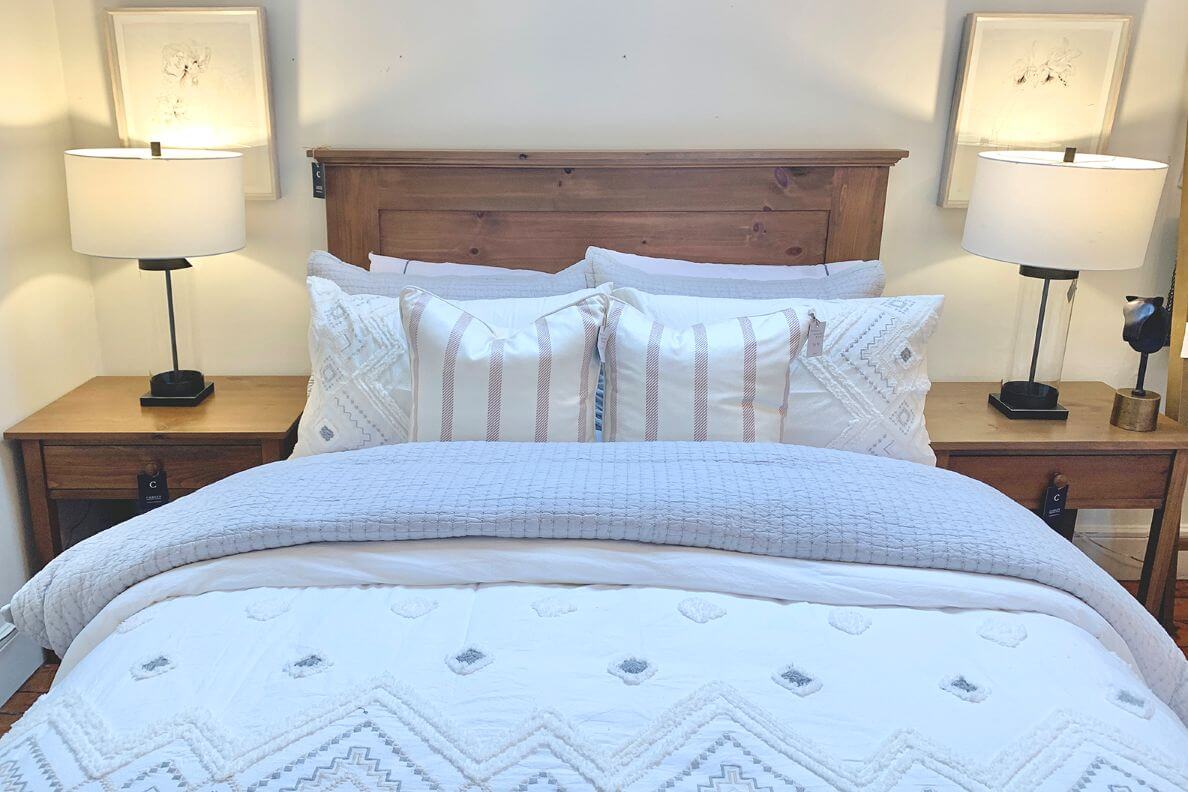 Bedroom with a wooden bed and matching nightstands, lamps, and decorative pillows.