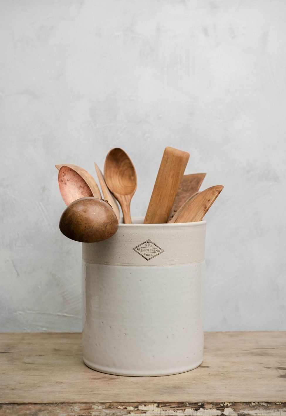 Set of wooden spoons in a white ceramic utensil pot on a wooden surface with a light gray background